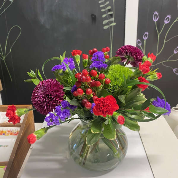Mixed bouquet in a round glass vase with red, purple, and green blooms
