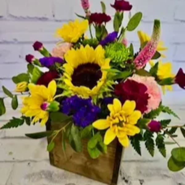 Mixed bouquet with sunflowers, carnations, and purple blooms in a wooden box