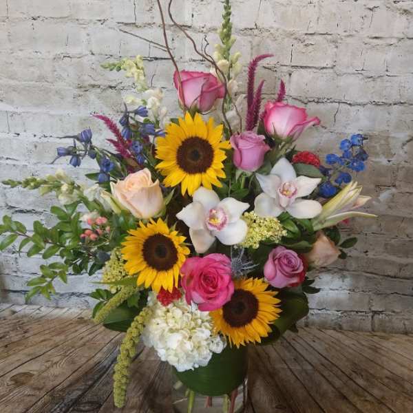 Mixed bouquet with sunflowers, pink roses, and white orchids in a glass vase