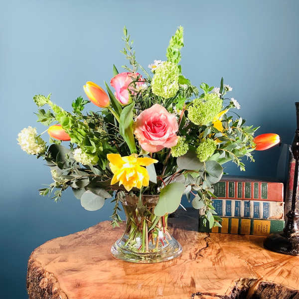 Mixed bouquet of pink roses, tulips, and yellow flowers in a clear glass vase