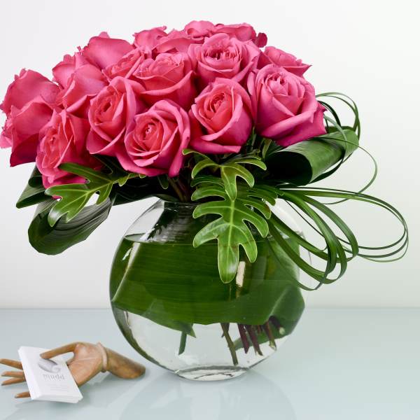 Pink roses arranged in a clear glass vase with tropical leaves