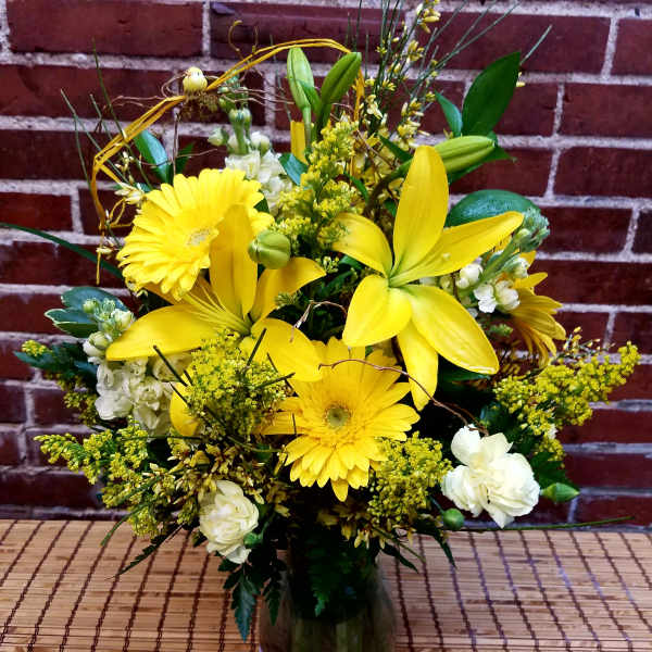 Yellow lilies and gerbera daisies in a glass vase