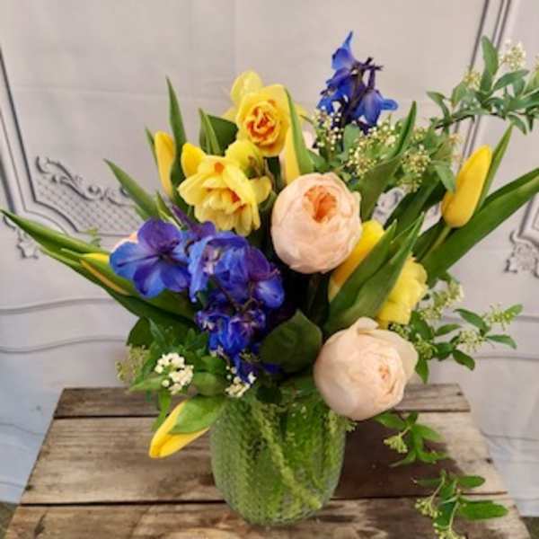 Mixed bouquet in a green glass vase with yellow, blue, and peach flowers