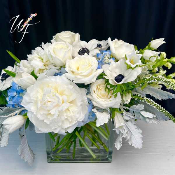 White floral arrangement in a square glass vase with blue accents
