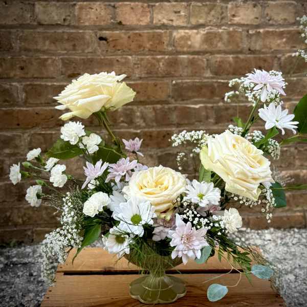 Cream roses and white daisies in a clear vase with pastel filler flowers
