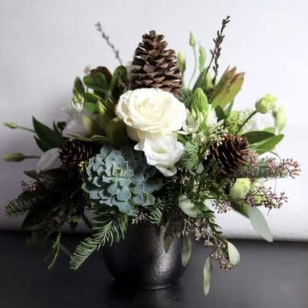 White roses and blue hydrangea in a black vase with pinecones