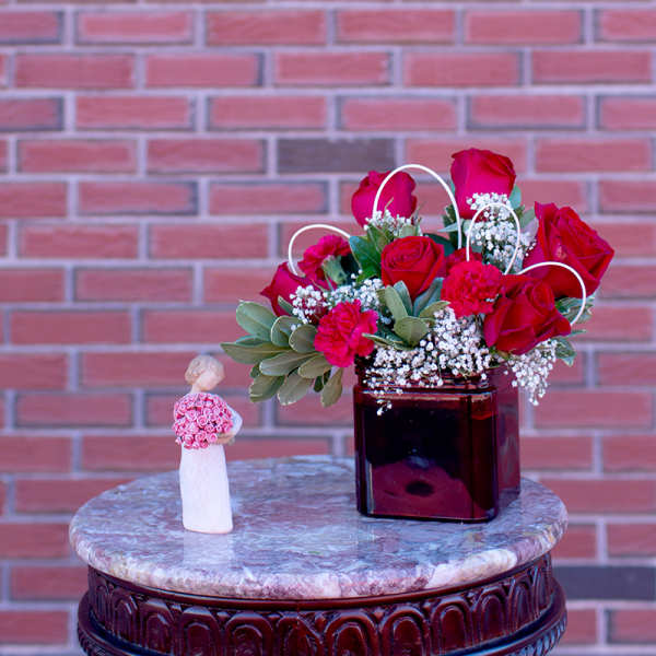 Red roses in a square vase beside a small figurine