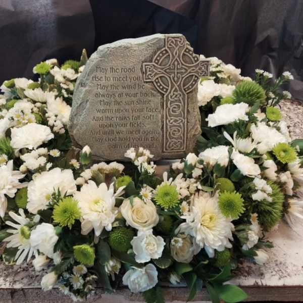 White floral wreath around a memorial stone with a Celtic cross