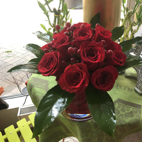 Red roses arranged in a glass vase with glossy leaves