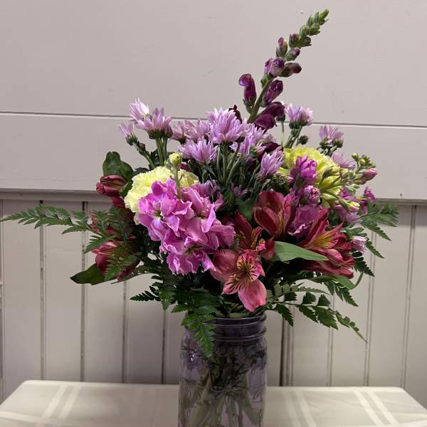 Mixed pink and purple flowers arranged in a glass jar vase