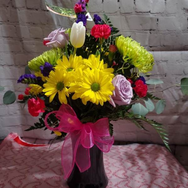 Bouquet of yellow daisies, roses, and tulips in a black vase with a pink bow