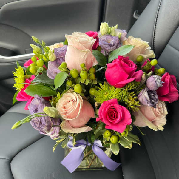 Bouquet of pink and lavender roses in a glass vase with a purple ribbon