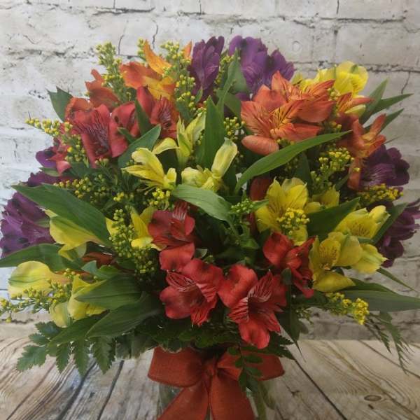 Mixed bouquet of red, yellow, orange, and purple flowers in a glass vase