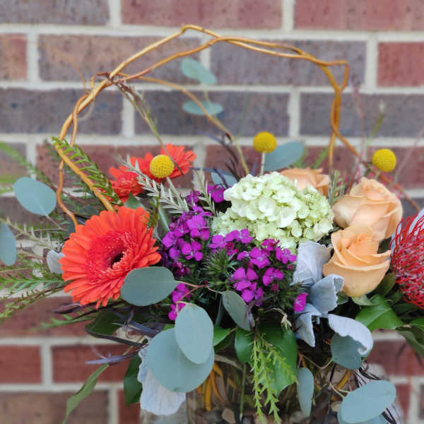 Mixed bouquet with orange gerbera daisies, peach roses, and purple blooms