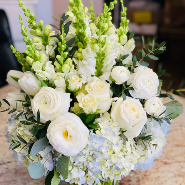 White bouquet with roses, ranunculus, snapdragons, and hydrangeas in a glass vase