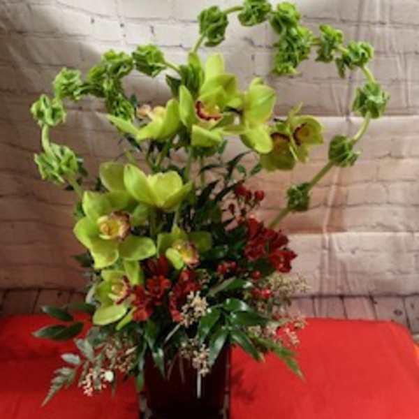 Tall floral arrangement with green orchids and red accents in a dark vase