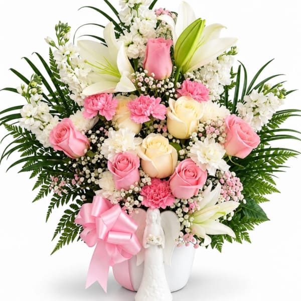 Pink and white floral arrangement in a white vase with a pink ribbon and angel figurine