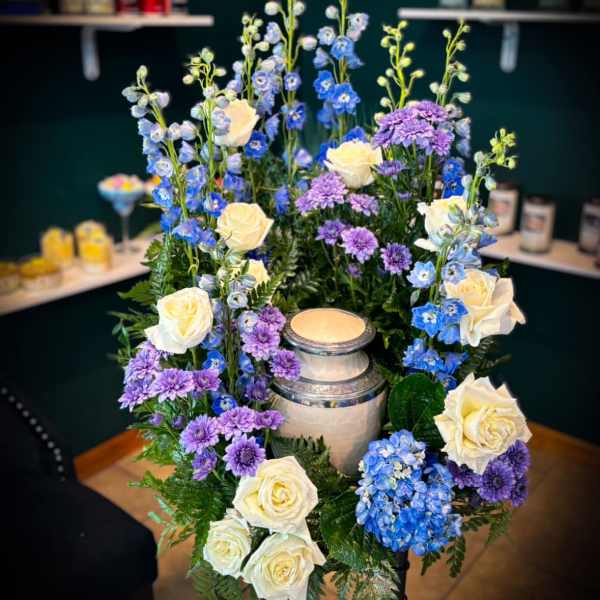 Tall floral arrangement with white roses, blue delphinium, and purple mums around a candle