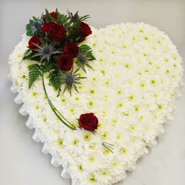 Heart-shaped white floral arrangement with red roses and greenery