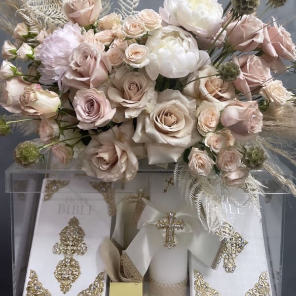 Blush and white rose arrangement above decorated white Bibles and a candle