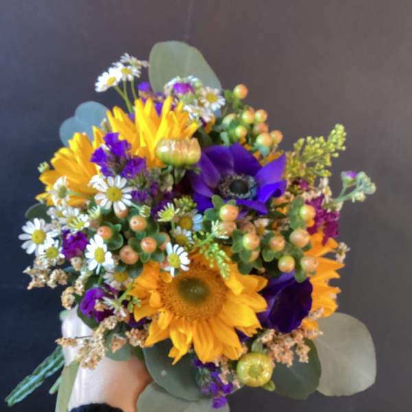 Handheld bouquet with sunflowers, purple blooms, and small white daisies