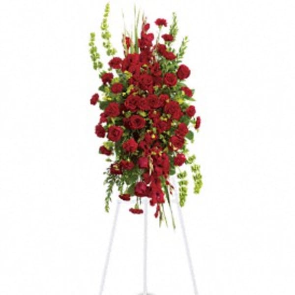 Tall standing spray of red roses and carnations on a white easel with vertical green accents