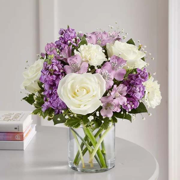 Bouquet of white roses and purple flowers in a clear glass vase