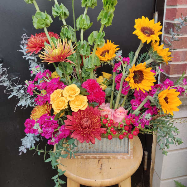 Colorful mixed flower arrangement in a rustic container with sunflowers and roses