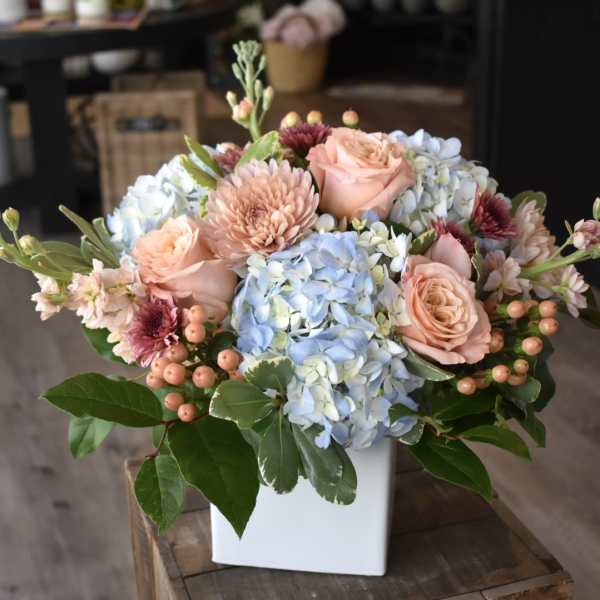 Bouquet of peach roses and blue hydrangeas in a white vase