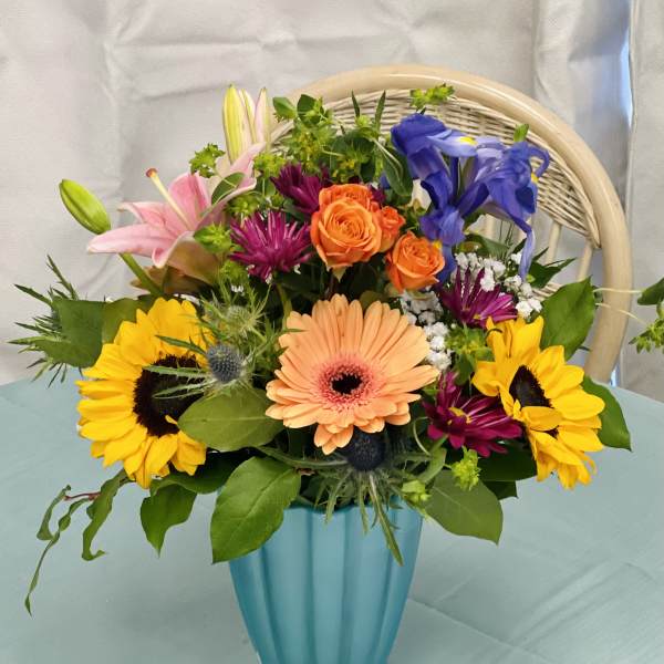 Mixed bouquet in a blue vase with sunflowers, roses, lilies, and gerbera daisies