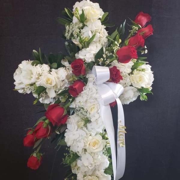 Cross-shaped floral arrangement with white flowers and red roses on a dark background