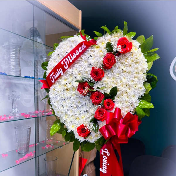 Heart-shaped white floral wreath with red roses and a red ribbon