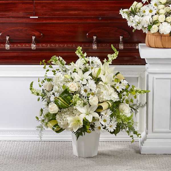 White funeral arrangement in a vase beside a casket