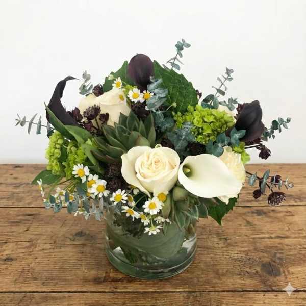 White roses and calla lilies in a glass vase with greenery