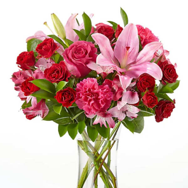 Bouquet of pink lilies, red roses, and carnations in a clear glass vase