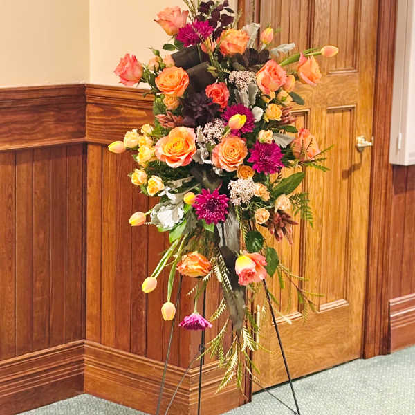 Tall floral standing spray with orange and pink blooms on an easel