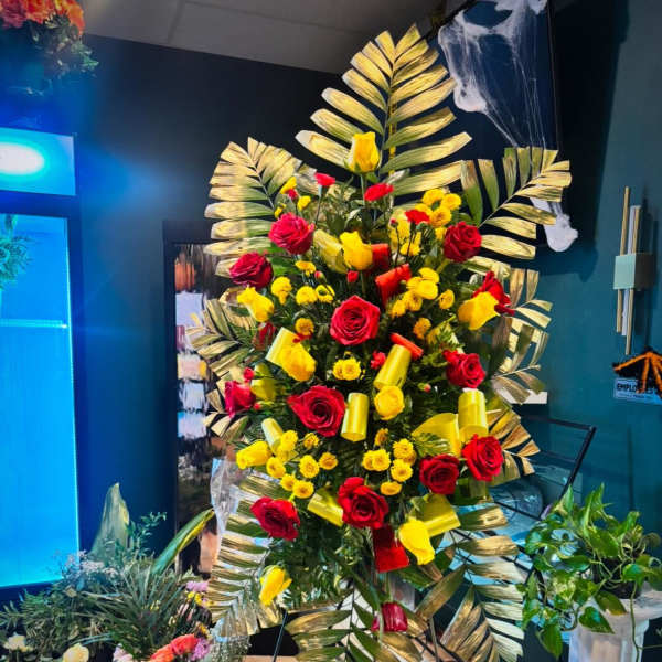 Tall floral standing spray with red and yellow roses and palm fronds