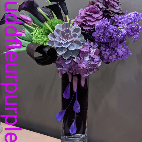 Purple floral arrangement with calla lilies, hydrangeas, and a succulent in a tall vase