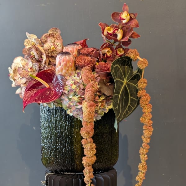 Tropical floral arrangement in a dark textured vase with burgundy orchids and anthurium