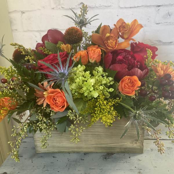 Mixed floral arrangement in a wooden box with orange and red blooms