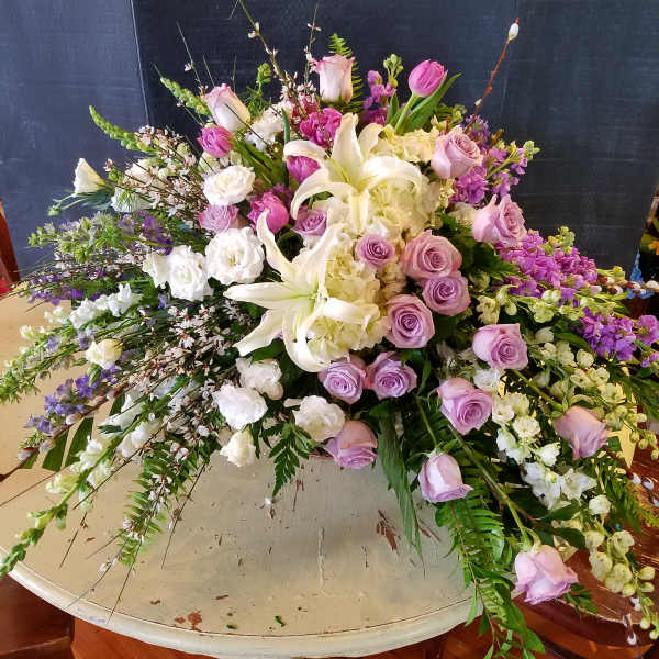 Large pastel floral arrangement with lilies, roses, and hydrangeas on a round table