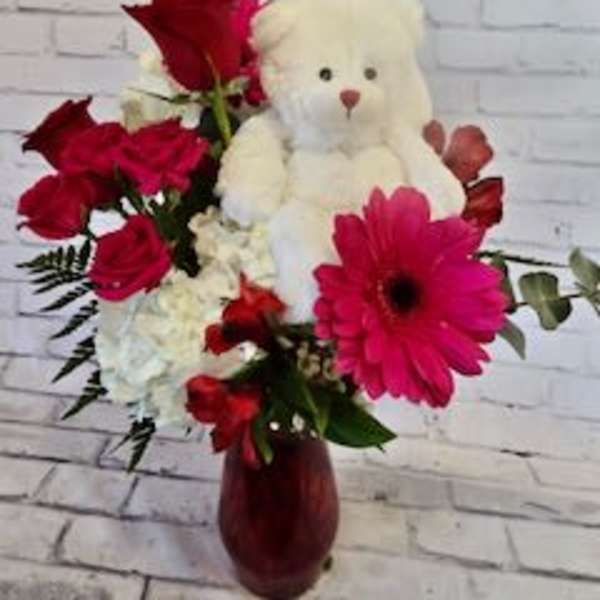 Red flowers arranged with a white teddy bear in a vase