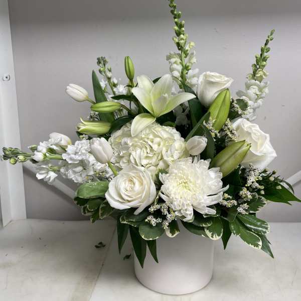 White floral arrangement in a round white vase with lilies and roses