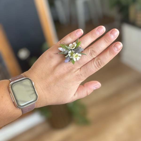 Hand wearing a small floral ring with white and lavender blossoms