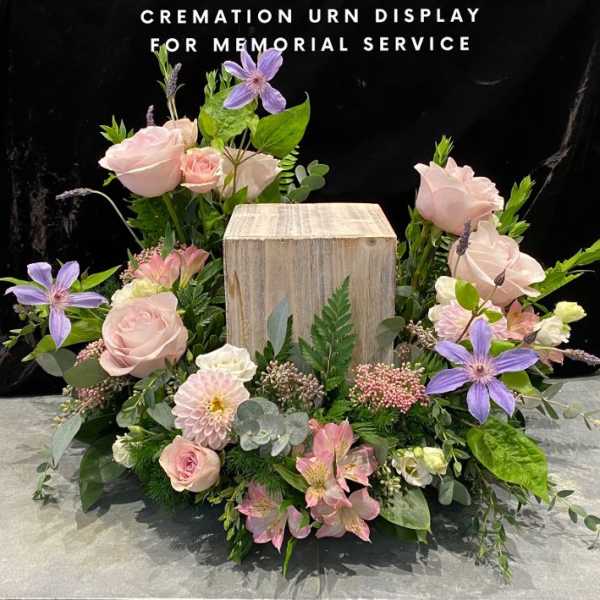 Floral cremation urn display with pink roses and purple clematis around a wooden urn box