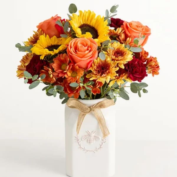 Bouquet of sunflowers, roses, and mums in a white vase with a ribbon