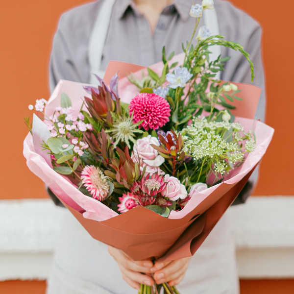 Handheld bouquet of pink and white flowers wrapped in peach paper