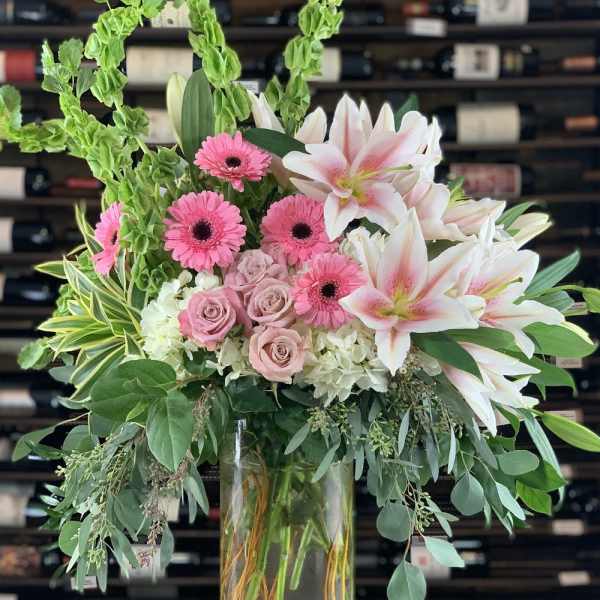 Pink gerberas and lilies in a clear glass vase with greenery
