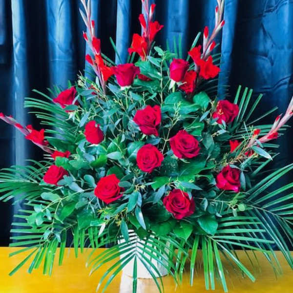 Large arrangement of red roses with tropical greenery in a white vase