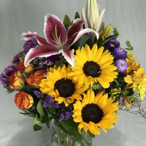 Bouquet of sunflowers, lilies, and roses in a glass vase